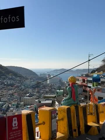 甘川洞文化村的小王子雕像，背景是山坡上的彩色房子與海
