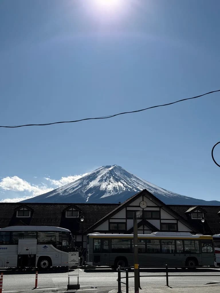 從河口湖站前看出去的富士山,山頂覆著雪,前面停著巴士